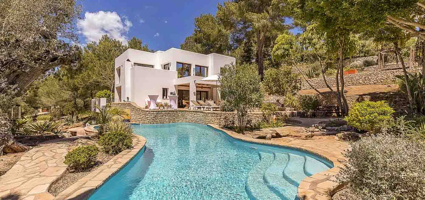 Serena villa en Ibiza con piscina curva rodeada de exuberante vegetación y senderos de piedra