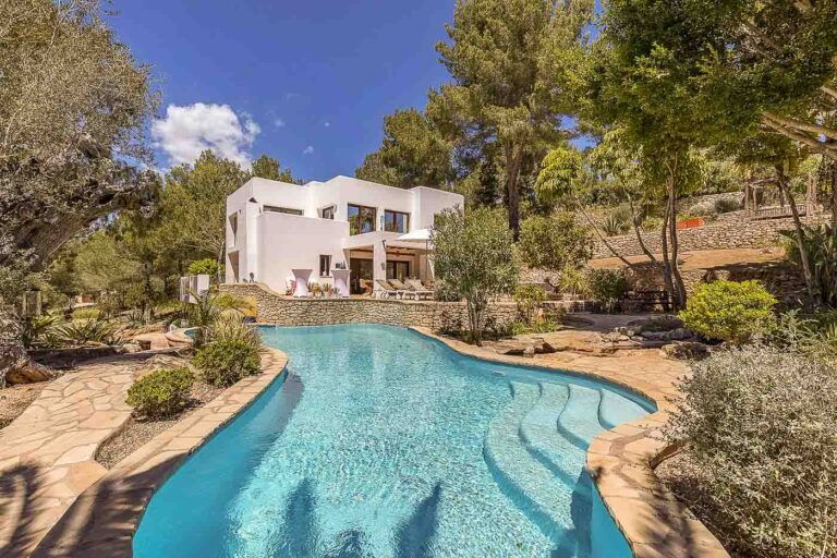 Serena villa en Ibiza con piscina curva rodeada de exuberante vegetación y senderos de piedra