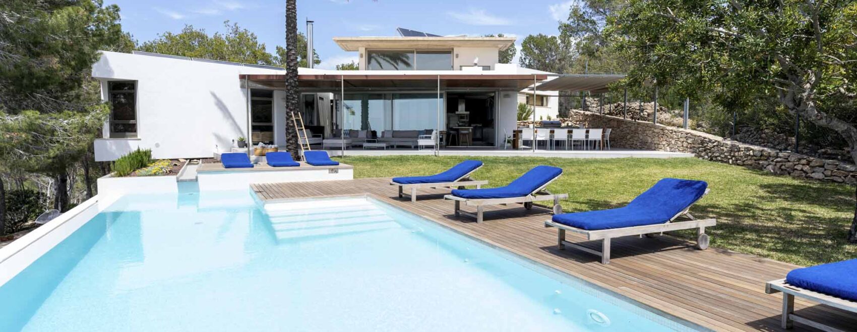 Luxurious Villa Sol Post in Ibiza with a large swimming pool, sun loungers, and lush garden, showcasing serene sunset views