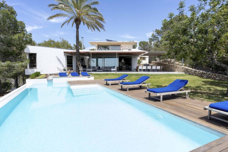 Luxurious Villa Sol Post in Ibiza with a large swimming pool, sun loungers, and lush garden, showcasing serene sunset views