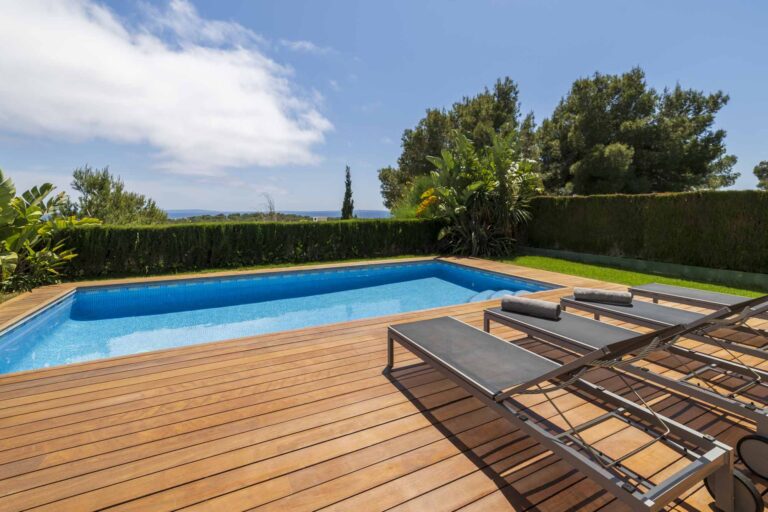 Lujosa piscina privada con agua azul cristalina, flanqueada por un espacioso deck de madera y cómodas tumbonas, con exuberante vegetación y una vista del horizonte del mar de fondo.