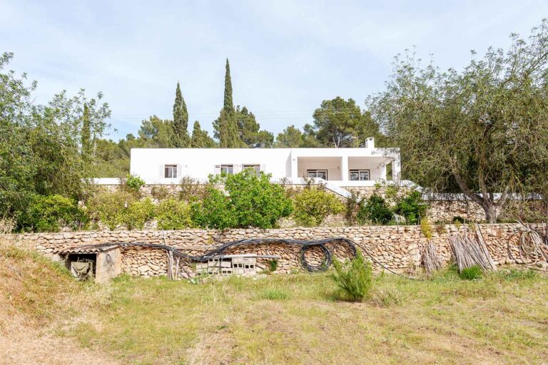 Secluded villa Roca Llisa Ibiza nestled in a rustic setting with lush greenery and stone wall accents, awaiting modernization