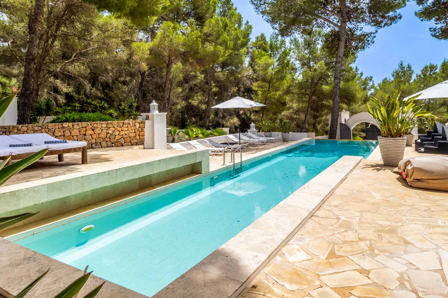 Gran piscina delante de la casa rodeada de vegetación mediterránea.