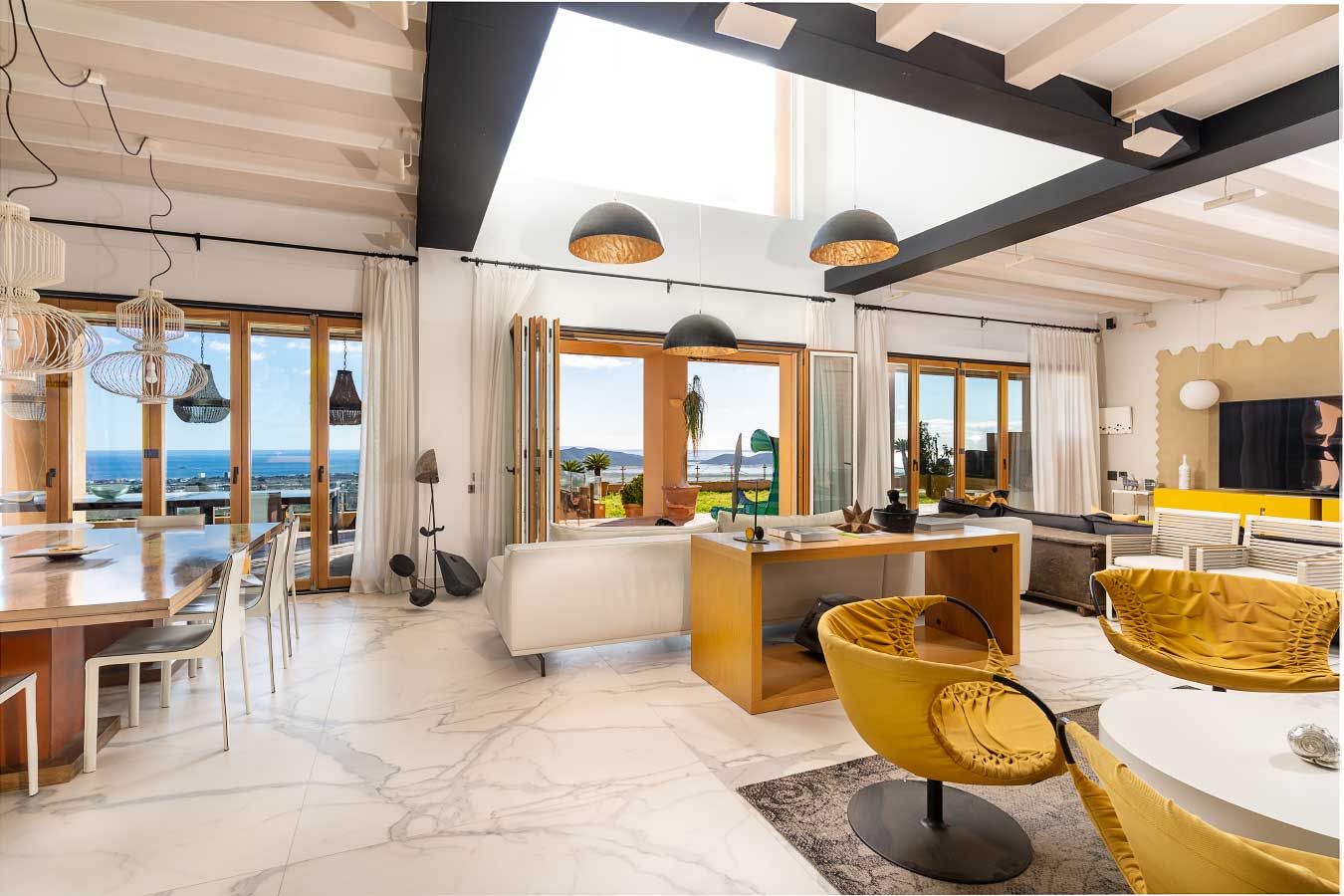 Amplio y espacioso salón con techos altos y amplios ventanales que ofrecen vistas al mar del sur en una villa de lujo en Ibiza